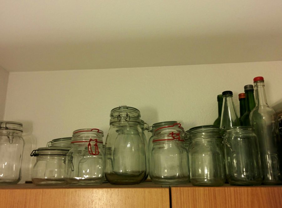 Øverst på skabet står et mindre lager af glaskrukker og -flasker klar til at blive fyldt med madvarer.